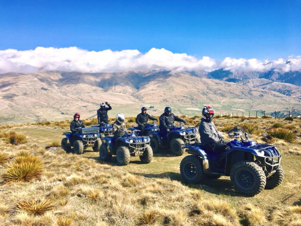 Six smiling people exploring a sunny Cardrona trail on quad bikes.